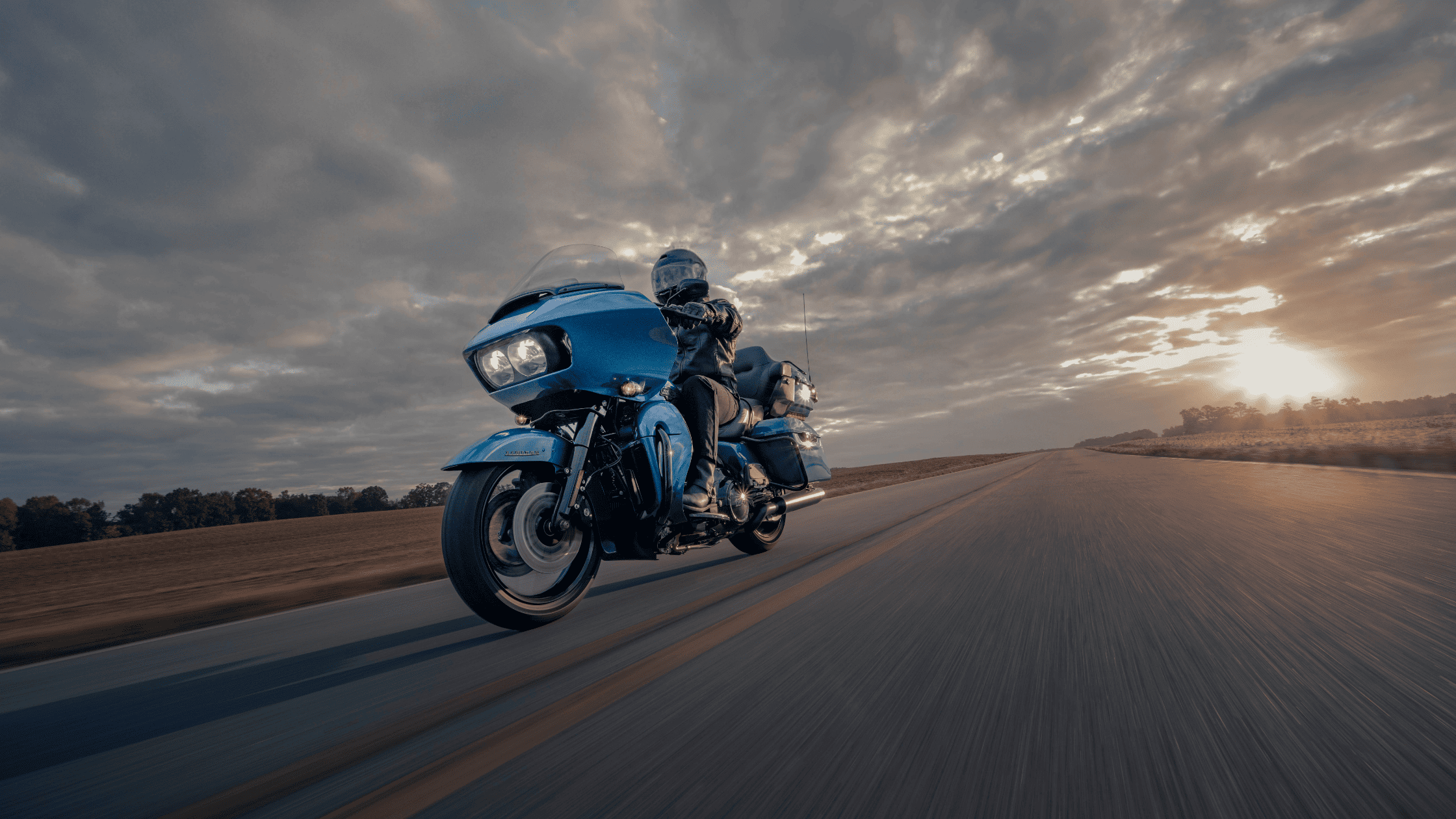 A person rides a blue 2024 Harley-Davidson® Road Glide® Limited motorcycle on a scenic road.