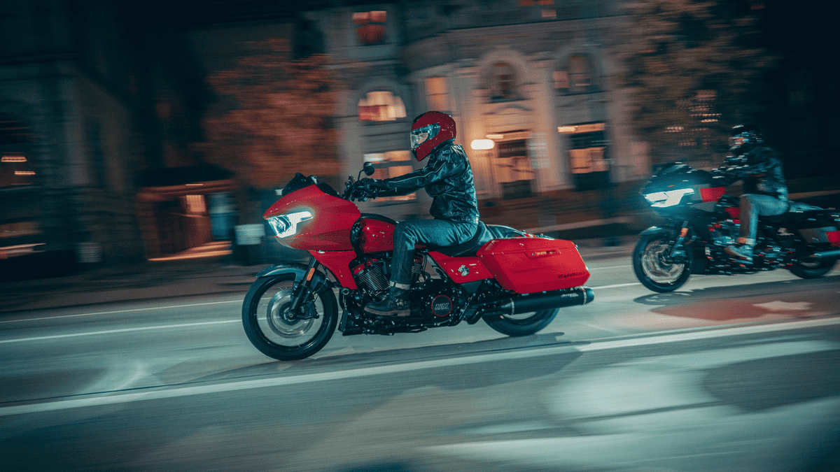 Two riders cruising through city streets on the 2025 Harley-Davidson® CVO™ Road Glide® ST near Missouri City, TX, highlighting its aggressive stance and bold red finish.