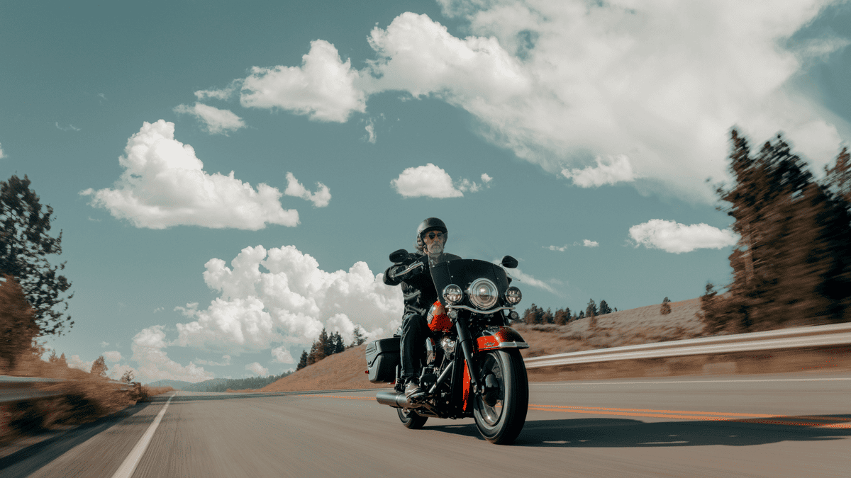 Rider cruising on a 2025 Harley-Davidson® Heritage Classic with windshield and saddlebags, captured on a scenic road near Bellaire, TX under clear skies.