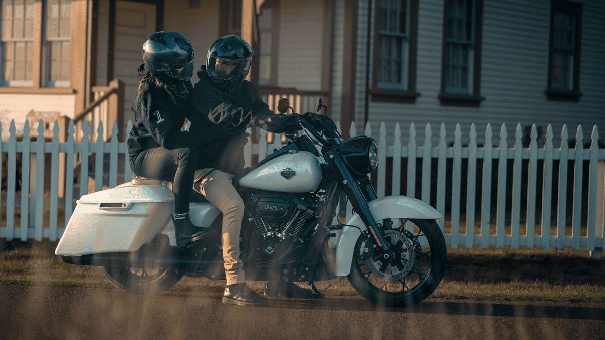 Rider and passenger enjoying the 2025 Harley-Davidson® Road King® Special in white, parked in front of a picket fence near Missouri City, TX, capturing classic touring vibes.