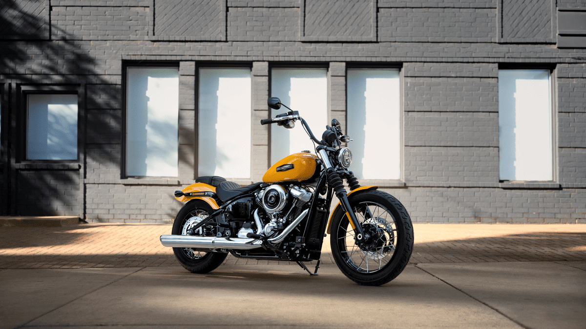 2025 Harley-Davidson® Street Bob® parked near a modern brick building in Missouri City, TX, featuring a sleek, stripped-down design and vivid yellow paint.