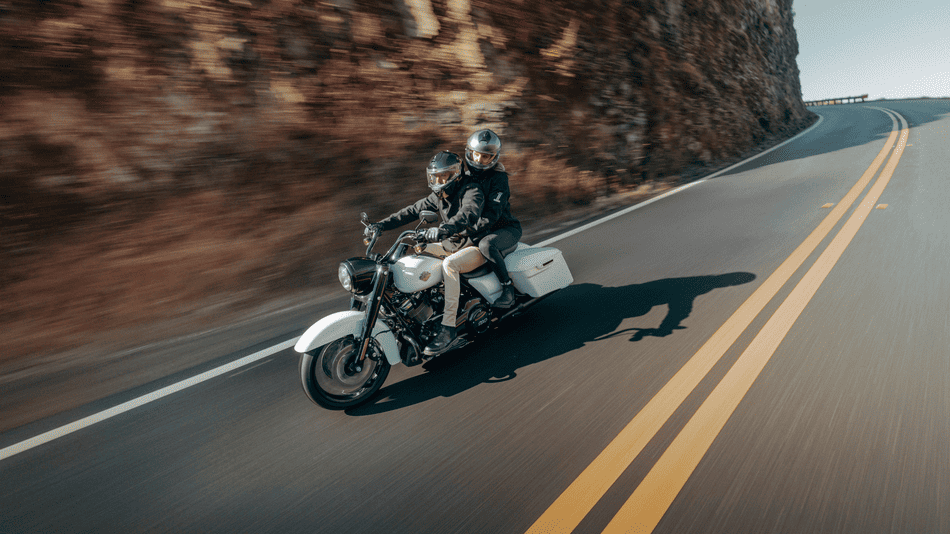 Two riders cruising on a white 2025 Harley-Davidson® Road King® Special along a winding mountain road near Missouri City, TX, showcasing touring potential and personalization options.