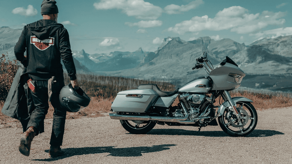 Rider walking toward a 2025 Harley-Davidson® Road Glide® parked in front of a mountain backdrop near Missouri City, TX, highlighting its long-distance touring appeal.