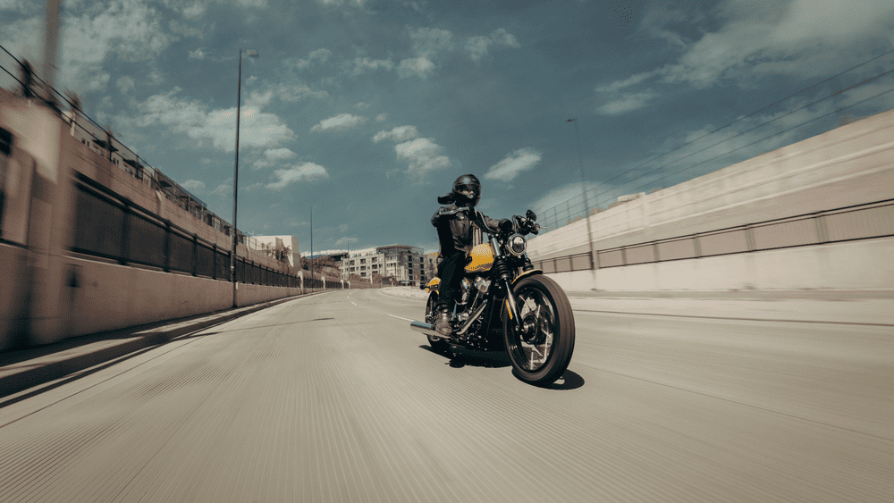 Rider cruising through an urban highway on the 2025 Harley-Davidson® Street Bob® near Missouri City, TX, emphasizing its stripped-down bobber style and mid-mounted controls.